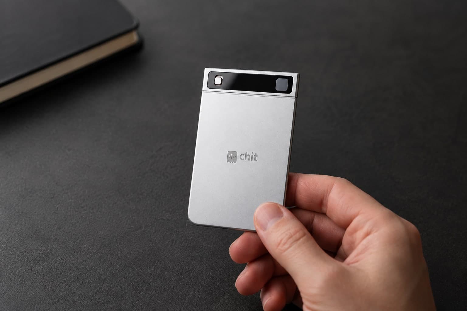Product visualization of silver chit one held beside a notebook