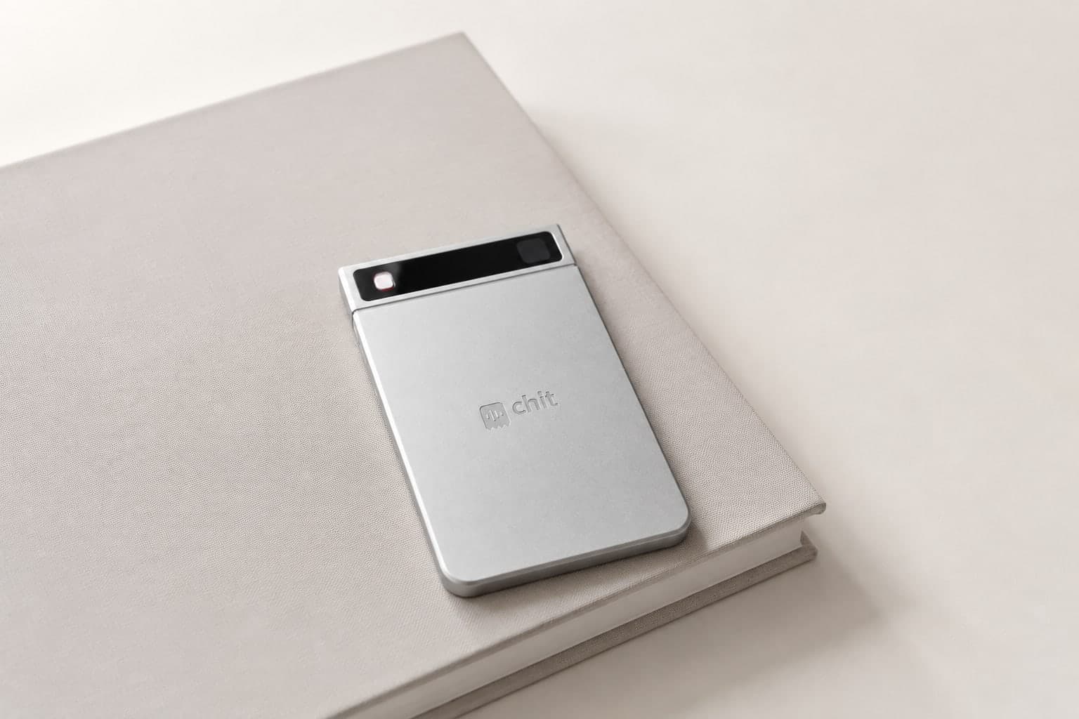Product visualization of silver chit one resting on a linen notebook in daylight